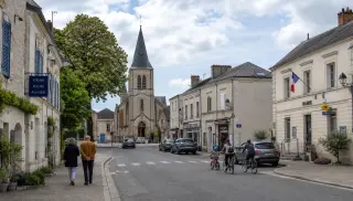 Rue calme dans un village de campagne avec maisons anciennes, mairie, église et habitants, illustrant l'ambiance d'un bourg du Maine-et-Loire.